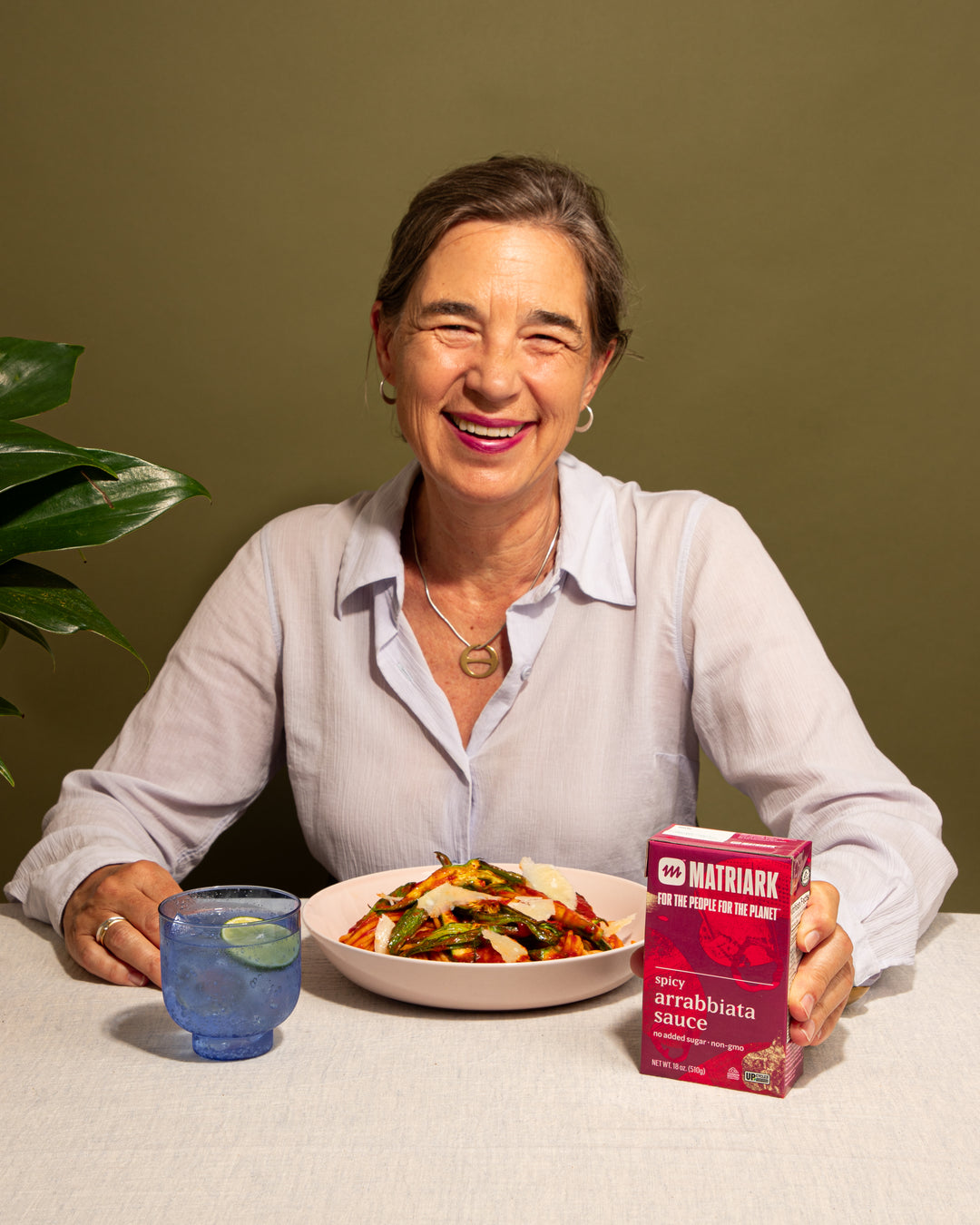 Matriark's founder, Anna Hammond, sits at a table with a plate of pasta, holding Matriark Spicy Arrabbiata.