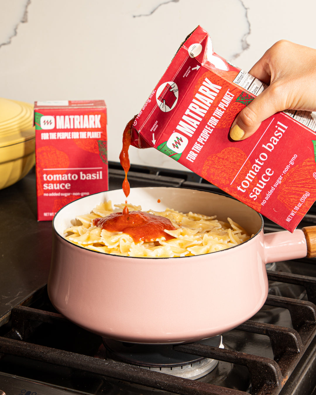 Matriark Tomato Basil sauce being poured into a pot with bow tie pasta