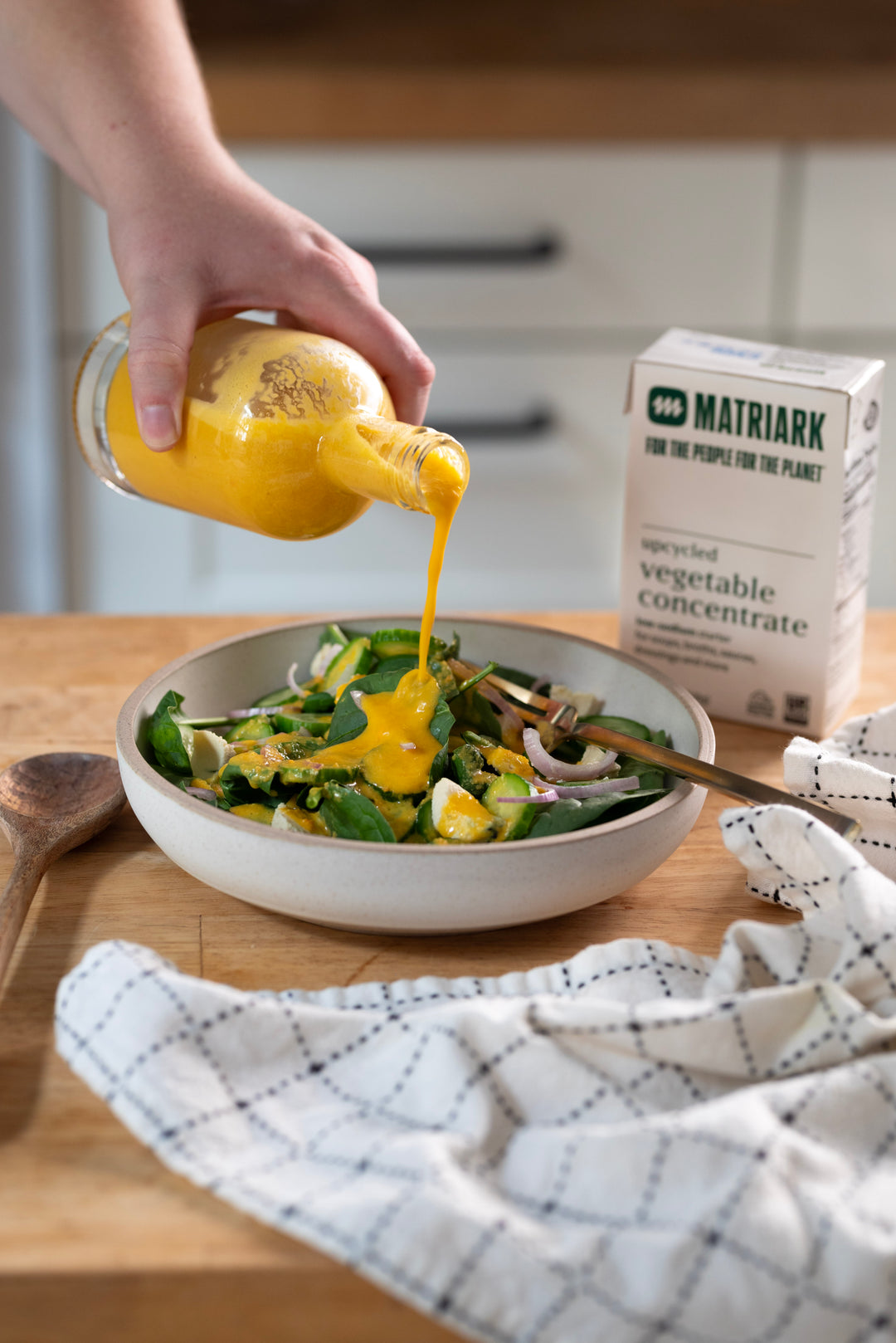 Dressing made with Matriark's Upcycled Vegetable Concentrate being poured over a salad that is sitting on a countertop.