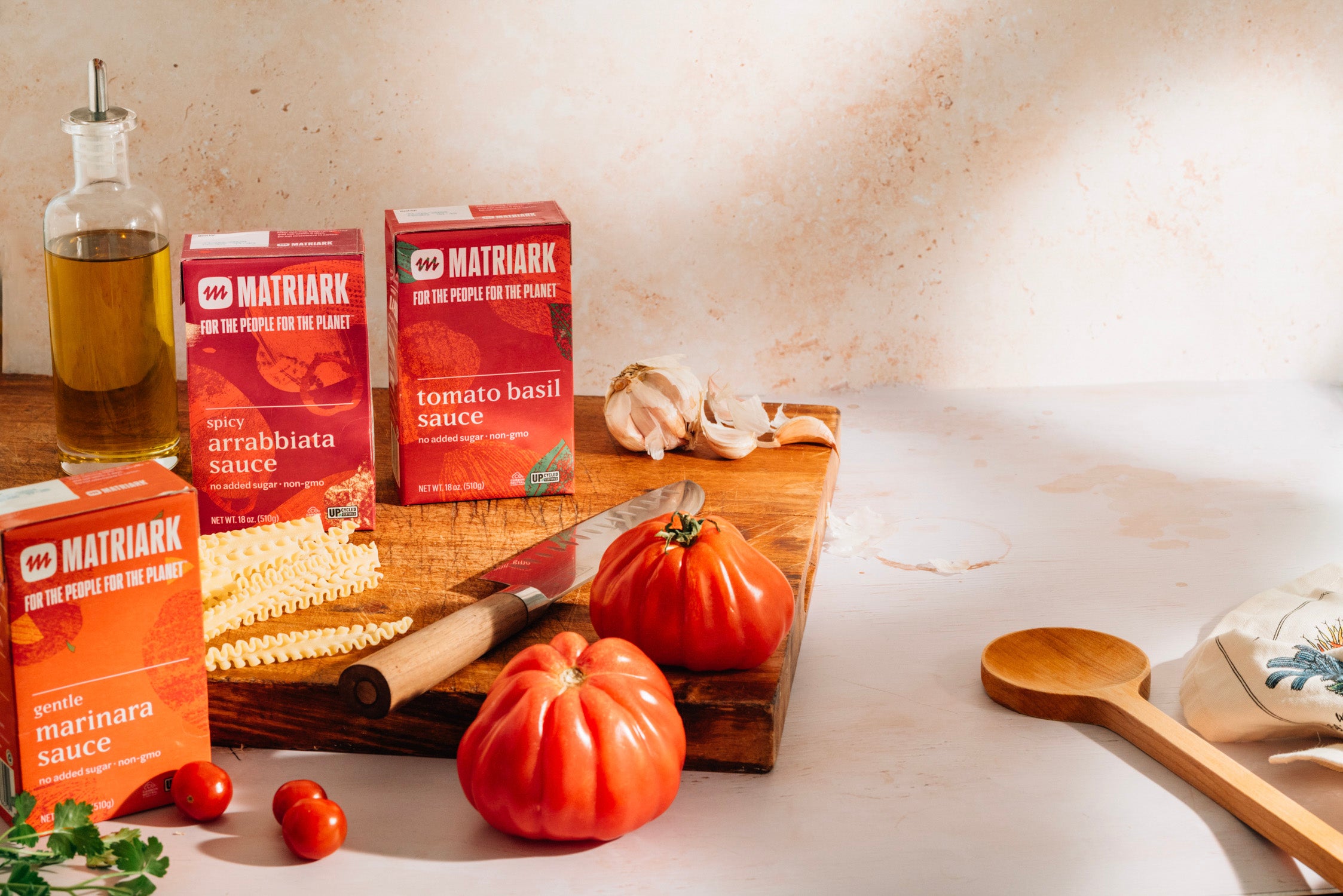 Matriark's Upcycled Sauces on a cutting board on a countertop, with tomatoes, garlic and pasta around them.